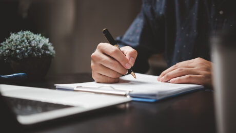Hand holding pen writing paperwork business document financial investment or signature contract job and insurance on desk.